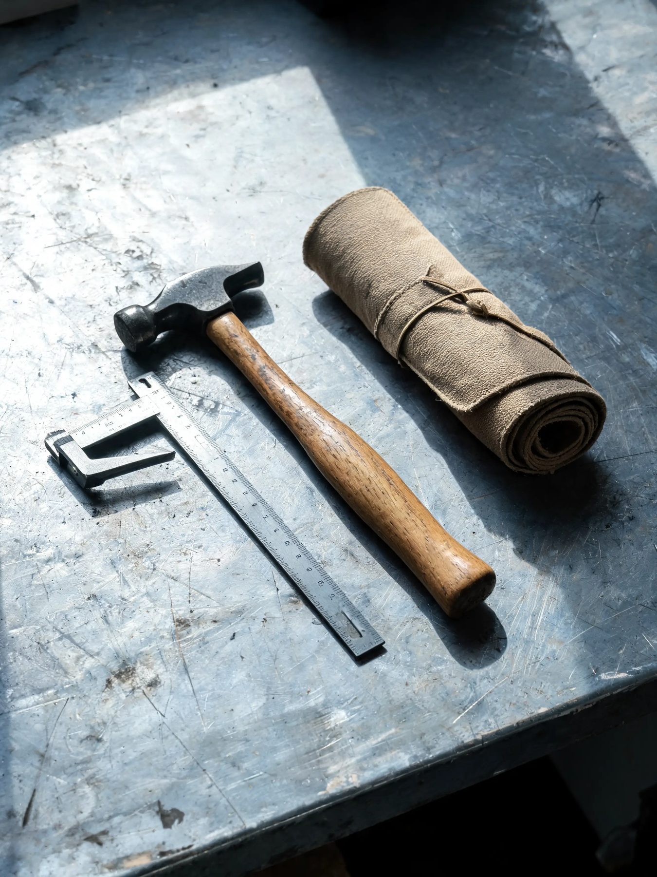 Hammer, combination square and canvas tool roll on a scarred steel bench